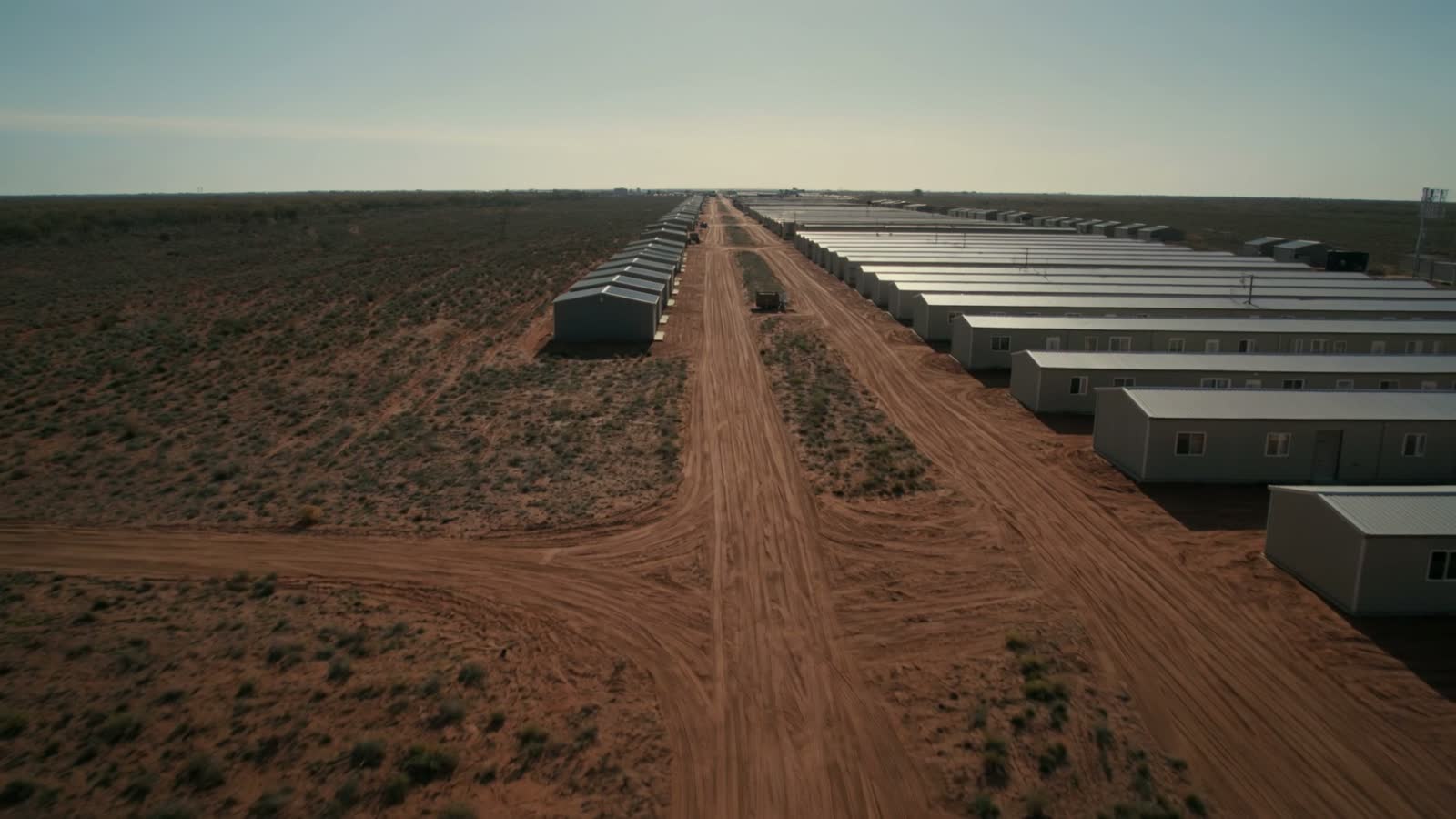 Rows of temporary site buildings on red earth at dawn