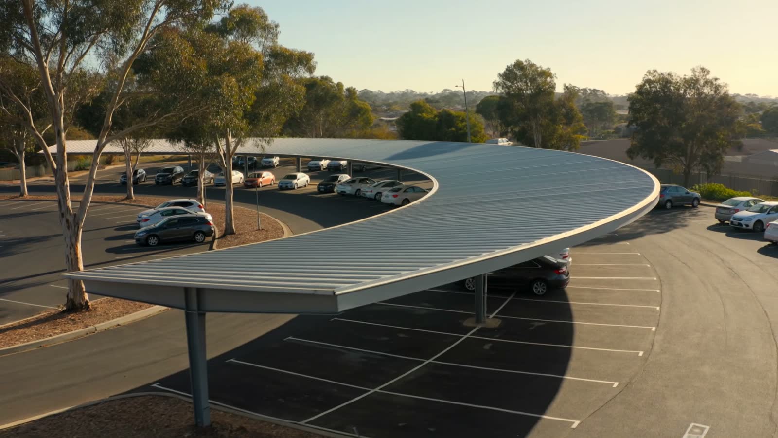 A curved public shade canopy in low golden light