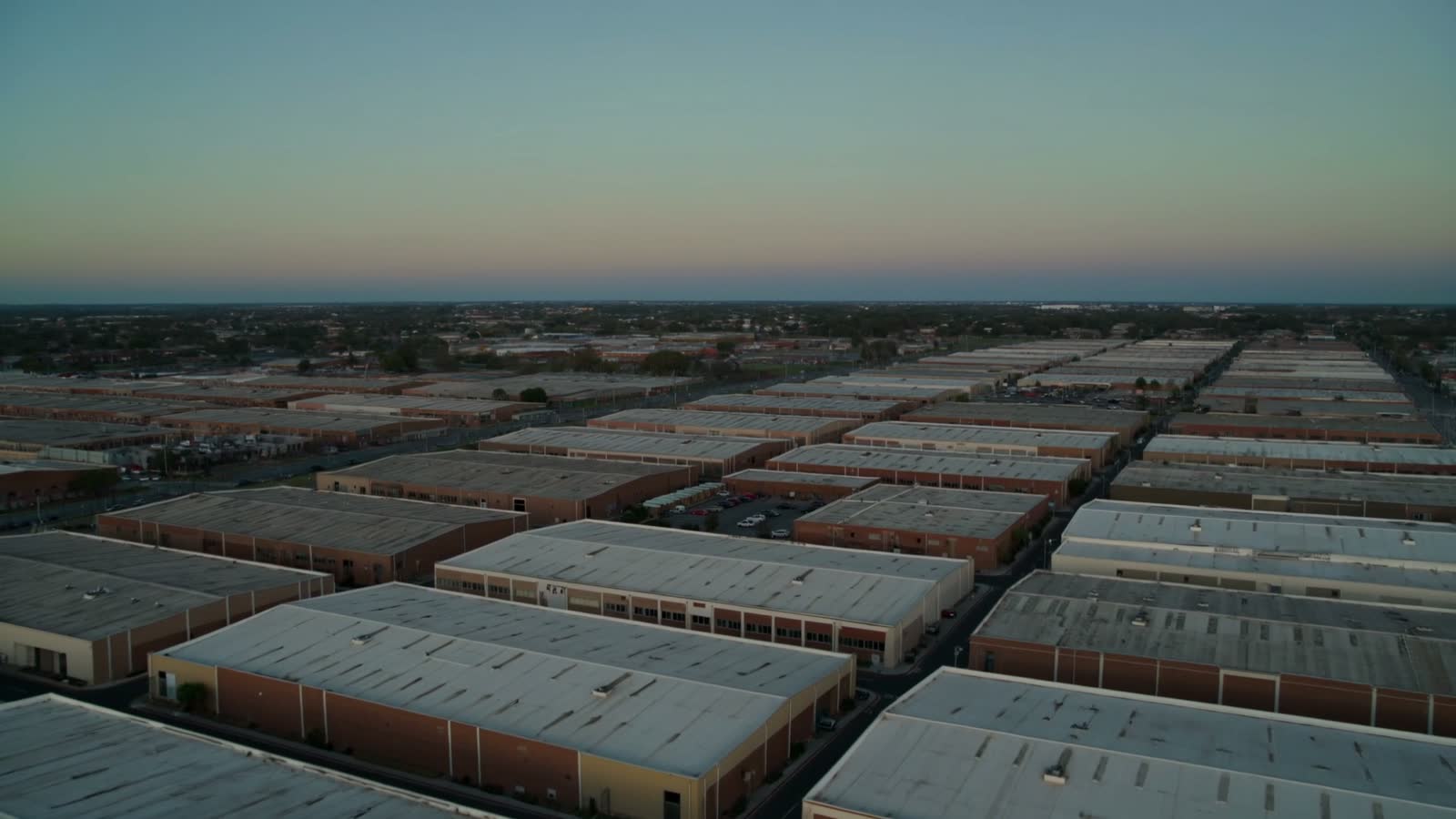 An industrial estate at dusk, hundreds of low roofs stretching to the horizon