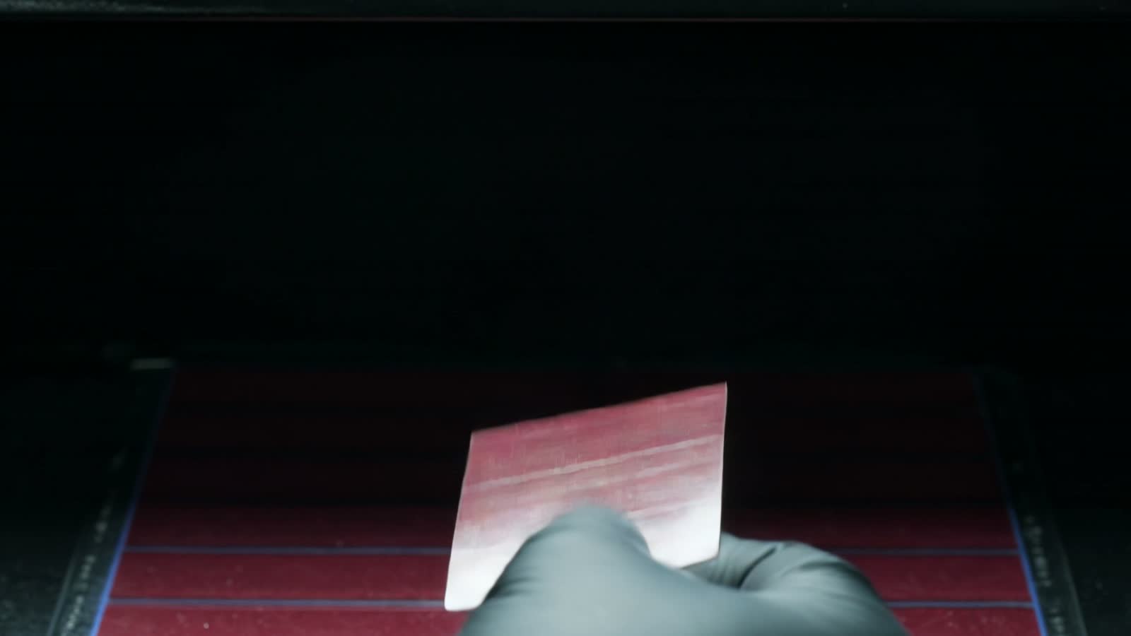 A gloved hand flexing a small sheet of Printed Solar