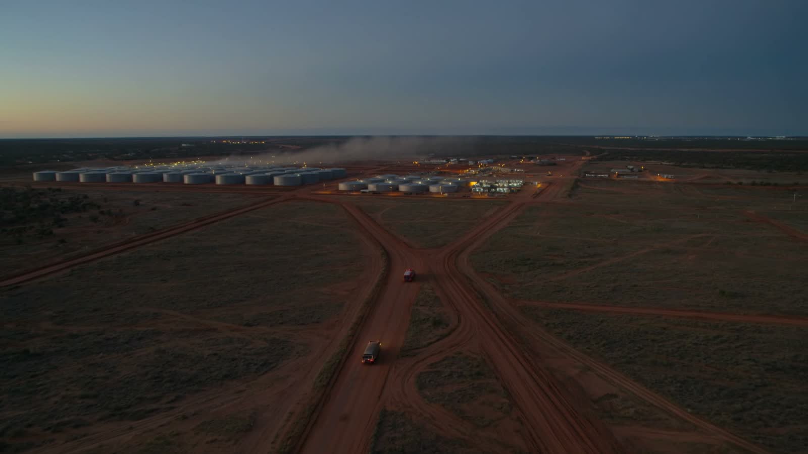 A remote Australian mine site at dusk, fuel tanks and accommodation buildings on red earth