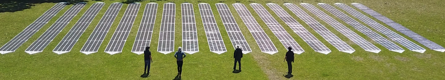 Rows of Printed Solar laid side by side on a grass field, with four people standing in front