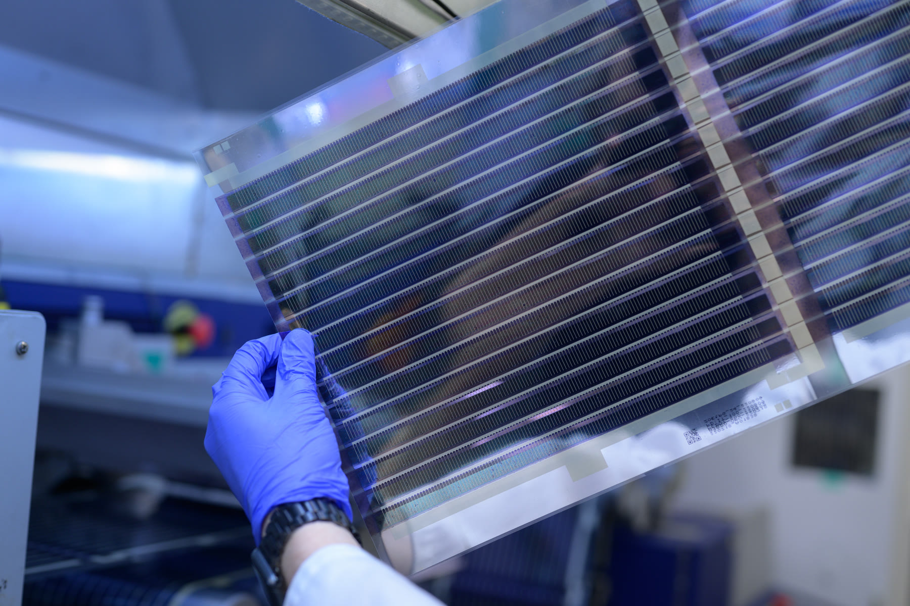 A blue-gloved hand holding a large Printed Solar sheet in the laboratory