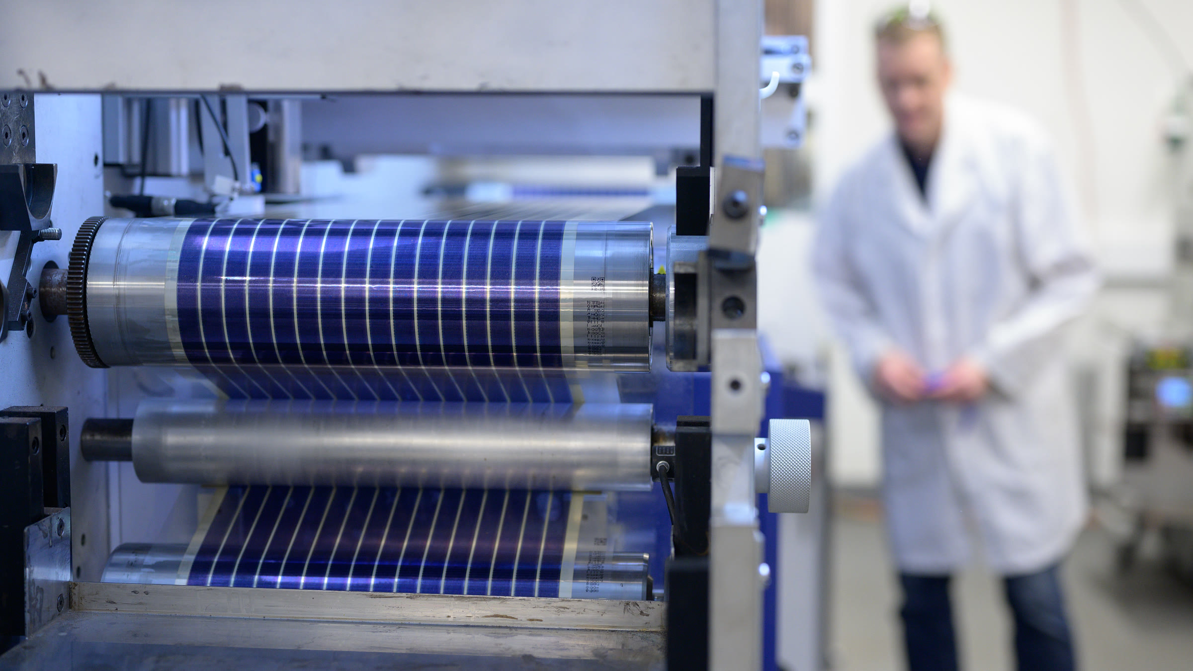 Blue Printed Solar cells running over the rollers of the pilot press, a researcher behind