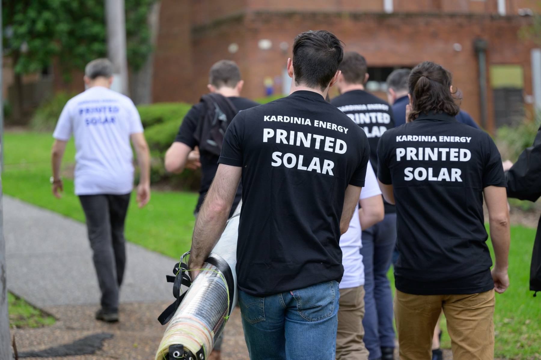The Kardinia team in Printed Solar shirts carrying a roll across a lawn